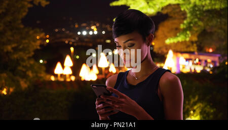 Hübsche junge schwarze Frau überprüft Ihr Handy Nachrichten außerhalb lächelnd Stockfoto