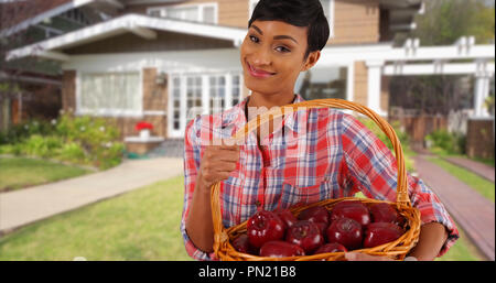 Lächelnd schwarze weibliche Holding Obstkorb außerhalb Home werfen Apfel in der Hand Stockfoto