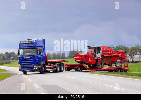 Blauer Scania R 560 Auflieger von H. Tuomola beginnt der Transport von einem roten Feldhäcksler an einem Tag des frühen Herbst kombinieren. Salo, Finnland - 2 September, 2018. Stockfoto