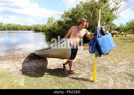 Ein junger Mann zieht seine alte Aluminium Kanu aus einem Fluss in die Everglades, an einem sonnigen Sommertag. Stockfoto