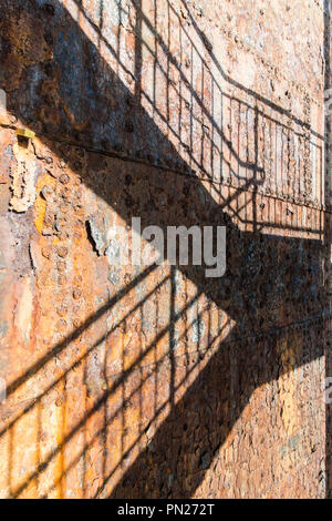 Rostige Stahlplatten auf einem alten Schiff, geknackt und mit abblätternder Farbe und rostige Nieten texturiert. Schatten von Metall Treppe warf auf der Oberfläche Stockfoto