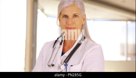 Ein älterer Arzt stellt für ein Portrait in Ihrem Büro Stockfoto