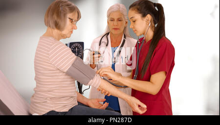 Ein älterer Patient hat ihren Blutdruck durch zwei medizinische Fachleute überprüft Stockfoto