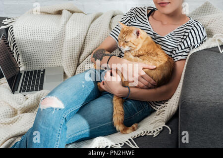 7/8 Schuß von Frau mit niedlichen Ginger cat und sitzen auf der Couch Stockfoto