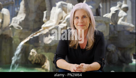 Glückliche Frau in Rom sitzt und lächelt vor Fiumi Brunnen Stockfoto