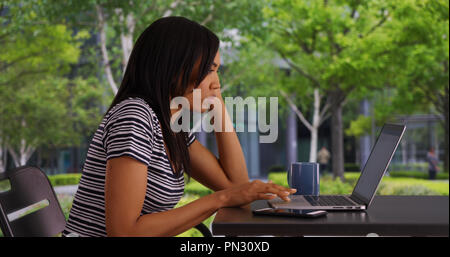 Attraktive schwarze Frau im freien Kaffee trinken und Surfen auf Ihrem Laptop Stockfoto