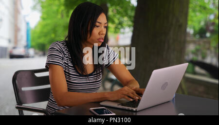 Hübsche schwarze Business woman mit Kaffee Schreiben von E-Mails auf Notebook Stockfoto