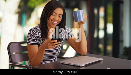 Süße schwarze Frauen sitzen im Freien scrollt durch Telefon lachend an Bilder Stockfoto