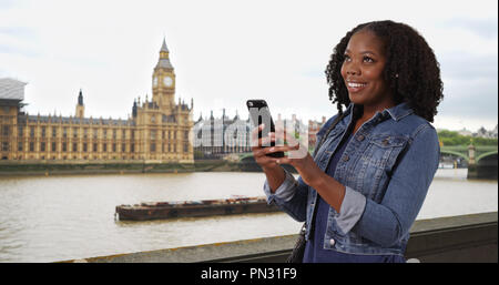 Hübsche schwarze Frau in London lächelt süß Text von Freund Stockfoto
