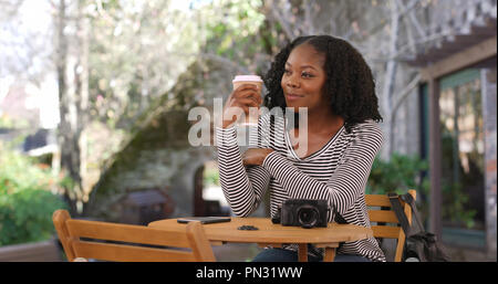 Attraktive schwarze Frau sitzt am Tisch im Freien Kaffee trinken Stockfoto
