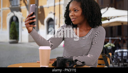 Lächelnd schwarze Frau sitzt an Outdoor Cafe in Rom selfie mit Handy Stockfoto
