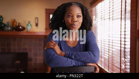 Lächelnd Portrait von hübsche schwarze Frau sitzt nach hinten in den Sessel zu Hause Stockfoto