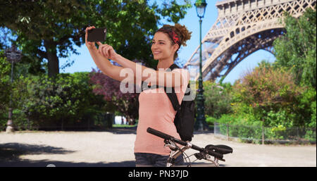 Kaukasische brunette auf Radtour in Paris hört selfie in der Nähe von Eiffelturm zu nehmen Stockfoto