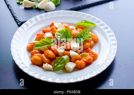 Gnocchi alla Sorrentina in Tomatensauce mit frischem Basilikum und Mozzarella Kugeln auf einem weißen Teller auf schwarzem Hintergrund serviert. Traditionelle it Stockfoto