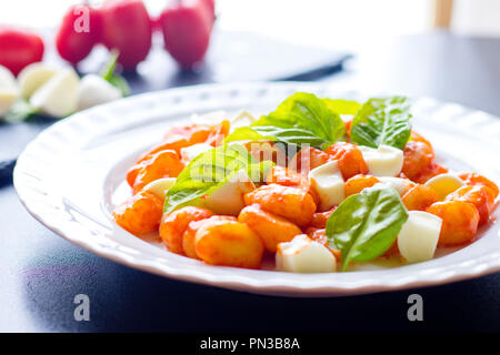 Gnocchi alla Sorrentina in Tomatensauce mit frischem Basilikum und Mozzarella Kugeln auf einem weißen Teller auf schwarzem Hintergrund serviert. Traditionelle it Stockfoto