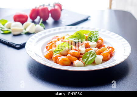 Gnocchi alla Sorrentina in Tomatensauce mit frischem Basilikum und Mozzarella in Scheiben geschnittene Kugeln auf einem weißen Teller mit Zutaten auf dem Schwarzen Brett bac serviert. Stockfoto