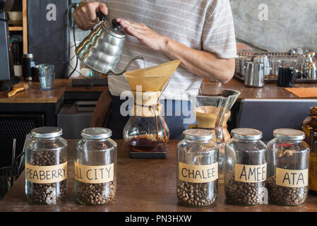 Barista Holding drip Topf und gießt Wasser auf gemahlenen Kaffee Bohnen in der papierfilter Für die Zubereitung von Filterkaffee im Cafe am Morgen. Kaffee dri Stockfoto