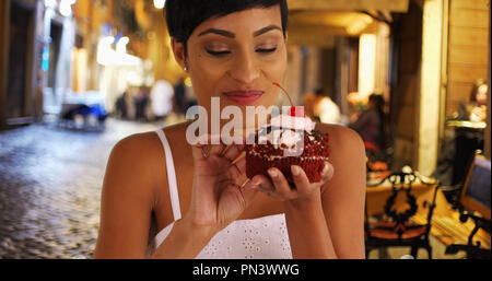 Schwarze Frau nimmt chaotisch Bissen von riesigen roten Samt Cupcake Stockfoto