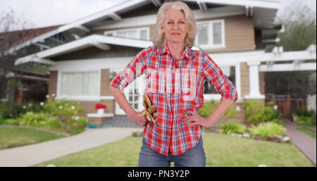 Frauenanteil in Flanell mit Gartenhandschuhe selbstbewusst vor dem Haus posing Stockfoto