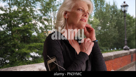 Ältere Frau, Ohrhörer und Kontrolle fitness Tracker vor dem Training Stockfoto