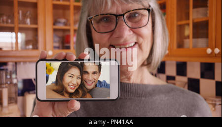 Alte Dame holding Handy Kamera, während videochatting mit Sohn und seine Freundin Stockfoto