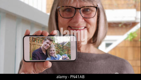 Sanfte ältere Frau zeigt Bild ihrer Tochter mit ihrem Freund am Telefon Stockfoto