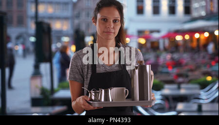 Unglücklich Kellnerin tragen Schürze und Durchführung Tablett mit Kaffee im Café im Freien Stockfoto