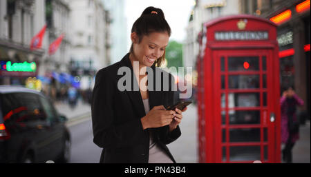 Lächelnd Business woman auf die London Street mit Telefonzelle texting mit Telefon Stockfoto