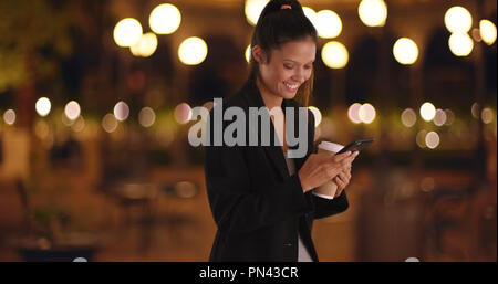 Die Frau im schwarzen Blazer Text Messaging und lächelnd in der Nacht Stockfoto