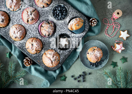 Blueberry Muffins mit Zuckerguss in einem Backblech mit Weihnachtsschmuck rund, flach, Ansicht von oben Stockfoto
