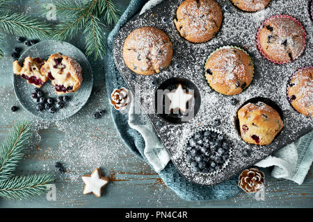 Blueberry Muffins mit Zuckerguss in einem Backblech mit Weihnachtsschmuck rund, flach, Ansicht von oben Stockfoto