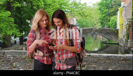 Paar Freundinnen mit Rucksäcken am Handy auf Brücke in Brügge suchen Stockfoto