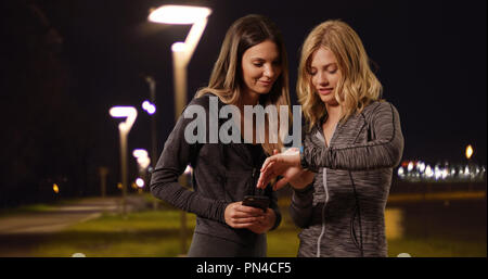Zwei attraktive Frauen timing Jog mit Stoppuhr und Smartphone außerhalb bei Nacht Stockfoto