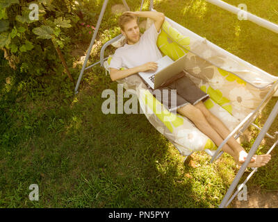 Junger Mann in casual liegen in der Couch mit dem Laptop auf Sommerferien Stockfoto