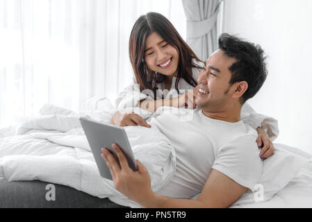 Gerne asiatische Paar mit Notebook und Tablet-PC zusammen auf dem Bett zu Hause, Lifestyle Konzept. Stockfoto