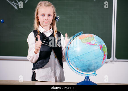 Schule Mädchen mit Globus im Klassenzimmer Tafel auf Hintergrund Stockfoto