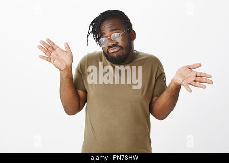Er weiß nichts. Portrait von ahnungslos ahnungslos cute afrikanisch-amerikanischen Bruder in Olive t-shirt und Brillen, zuckend und Verbreitung Palmen mit befragten Ausdruck, unsicher und verwirrt Stockfoto