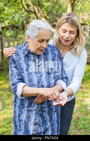 Deaktiviert alte Dame unter medizinische Pillen aus der freundliche Helfer Hand. Die Zeit im Garten Stockfoto