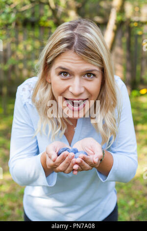 Glückliche junge Frau im Garten halten eine Handvoll reife Pflaumen Stockfoto