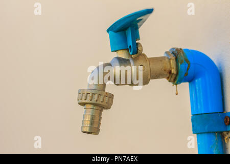 Grunge bronze Feld Wasserhahn mit blauem PVC-Rohr in weißen Wand Hintergrund verbunden. Stockfoto