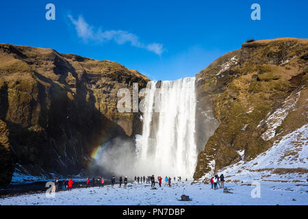 Touristen und Rainbow an spektakulären Skogar Wasserfall - skogar - im Süden Islands mit sprudelnden Gletscherschmelze Gewässern Stockfoto