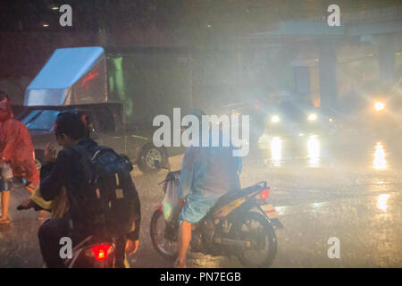 Bangkok, Thailand - 6. Juli. 2017: Menschen tragen Helm und Regenmantel fahrt Motorrad im schweren Regen durch das Wasser auf der Straße während der Regenzeit. Tr Stockfoto