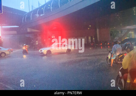 Bangkok, Thailand - 6. Juli. 2017: Menschen tragen Helm und Regenmantel fahrt Motorrad im schweren Regen durch das Wasser auf der Straße während der Regenzeit. Tr Stockfoto