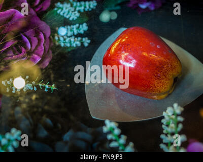 Schöne rote poison apple auf der Platte in der Nähe der roten Rosen und weißen Blüten. Stockfoto