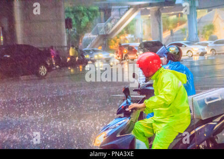 Bangkok, Thailand - 6. Juli. 2017: Menschen tragen Helm und Regenmantel fahrt Motorrad im schweren Regen durch das Wasser auf der Straße während der Regenzeit. Tr Stockfoto