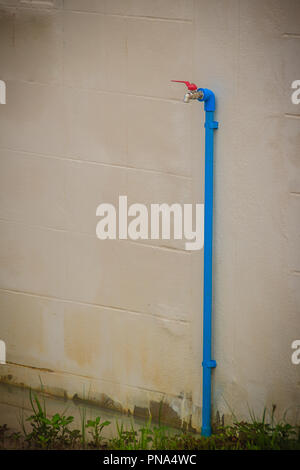 Grunge bronze Feld Wasserhahn mit blauem PVC-Rohr in weißen Wand Hintergrund verbunden. Stockfoto