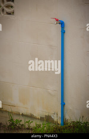 Grunge bronze Feld Wasserhahn mit blauem PVC-Rohr in weißen Wand Hintergrund verbunden. Stockfoto