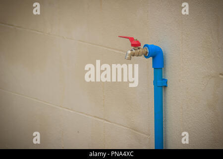 Grunge bronze Feld Wasserhahn mit blauem PVC-Rohr in weißen Wand Hintergrund verbunden. Stockfoto