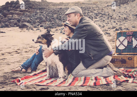Glückliches Paar mit netten Hunden Aufenthalt am Strand, Picknick enjoyng der Natur und der Beziehung. Vintage Farben und Filter für romantische und Reisen Stockfoto