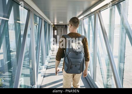 Anreise mit dem Flugzeug. Ansicht der Rückseite des jungen Mann mit Rucksack und Pass in der Hand beim Boarding am Flughafen. Stockfoto